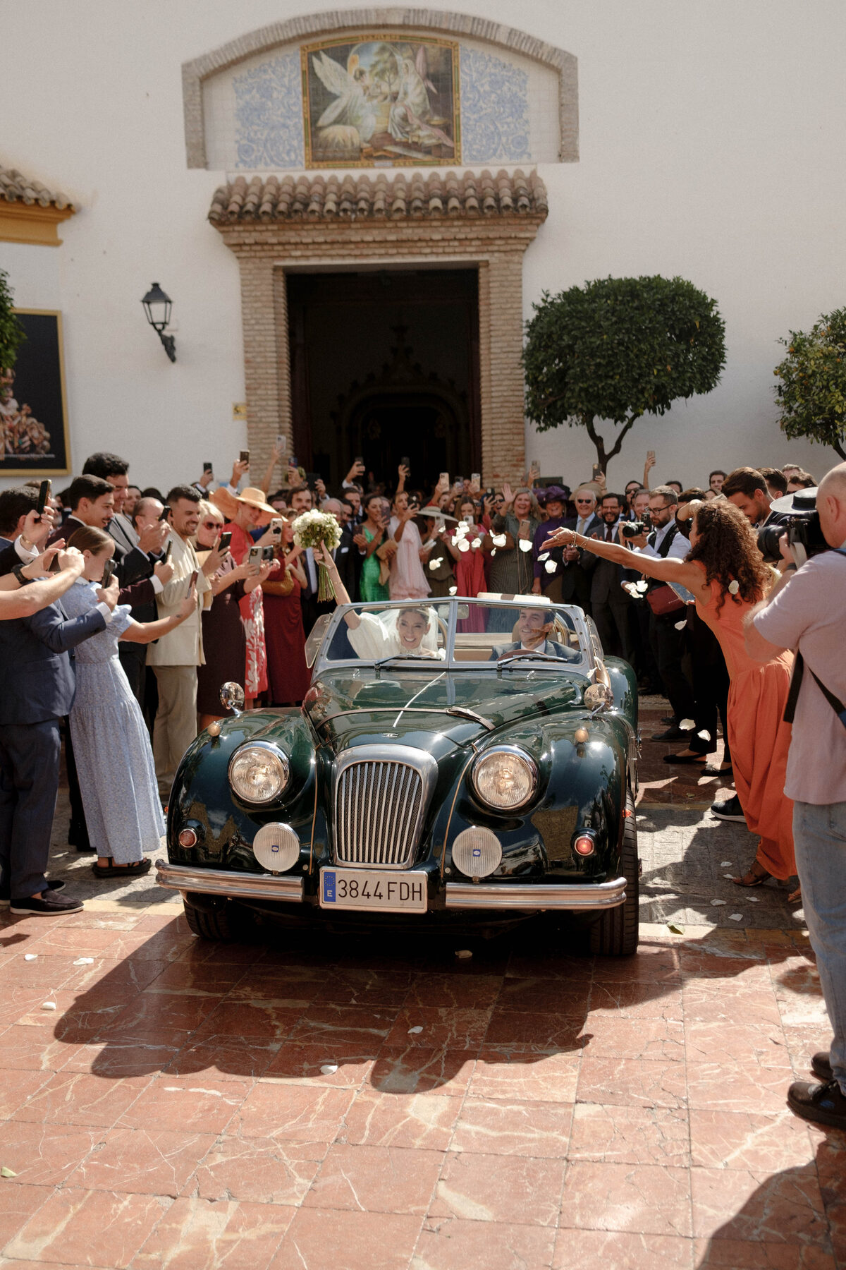 Newlyweds leaving the church in a vintage green convertible, guests cheering